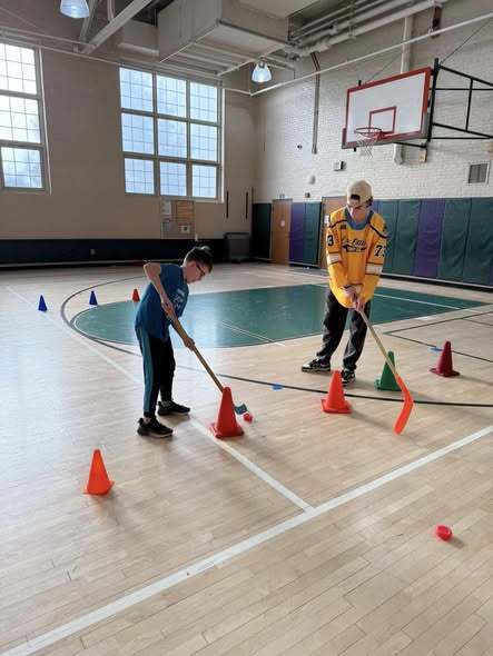 Kids playing hocky in a school gym with Erie Otters Hocky Players. 