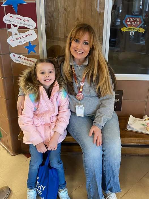 A student in a pink jacket sitting next to a a teacher in a gray quarter zip. 