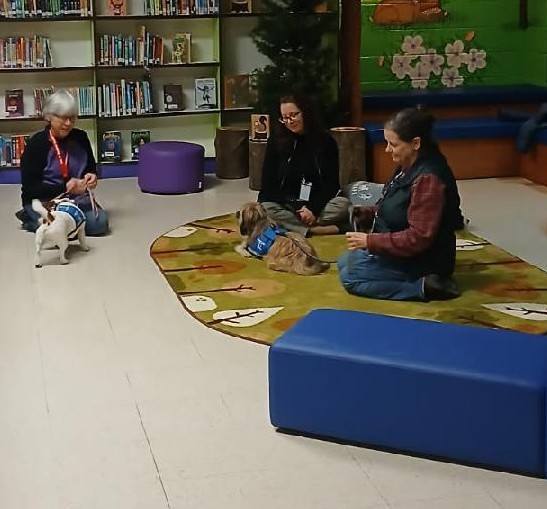 People sitting on the floor with two therapy dogs. 