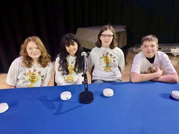 Four students sitting behind a table for the multicultural quiz bowl. 