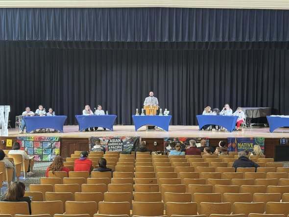 Multicultural Quiz Bowl contestants on stage at their tables while audience watches in auditorium. 