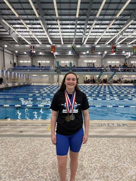 A young lady with two medals standing in front of a pool. 