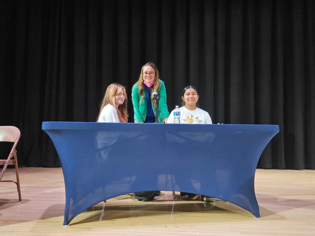 Two young ladies and an adult are behind a table at the multicultural quiz bowl.