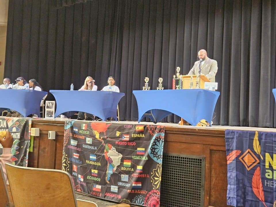 Multicultural Quiz Bowl contestants on stage at their tables.