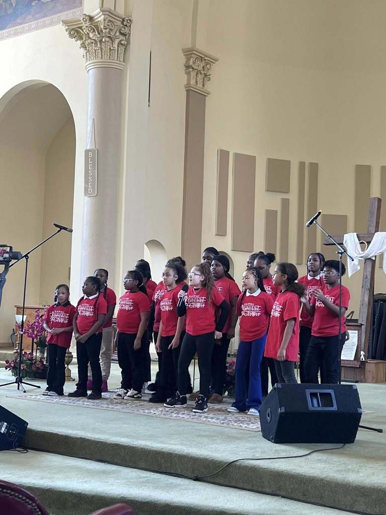 Group of students wearing matching red shirts are singing in a church. 