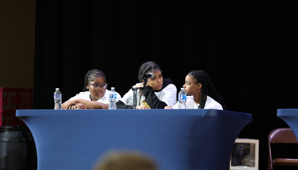 Students sitting behind a table and are competing in the multicultural quiz bowl. 