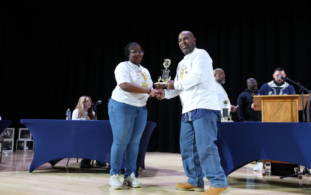 A student receiving a trophy and shaking a mans hand. 