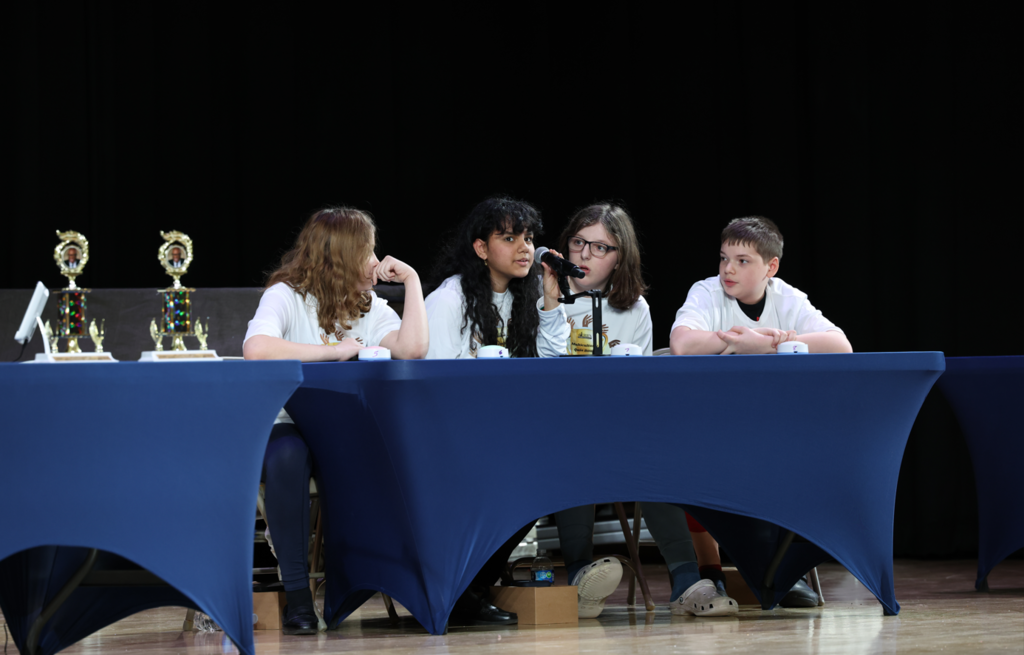 Students sitting behind a table and are competing in the multicultural quiz bowl. 