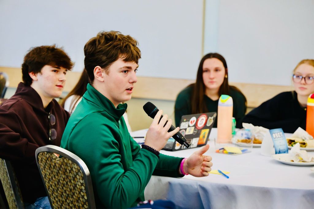 A student speaking into a microphone as others watch. 