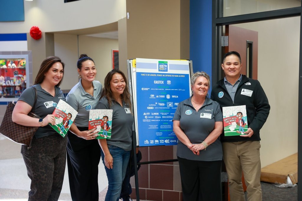 Five people in gray shirts and jeans stand behind a blue sign in a hallway.