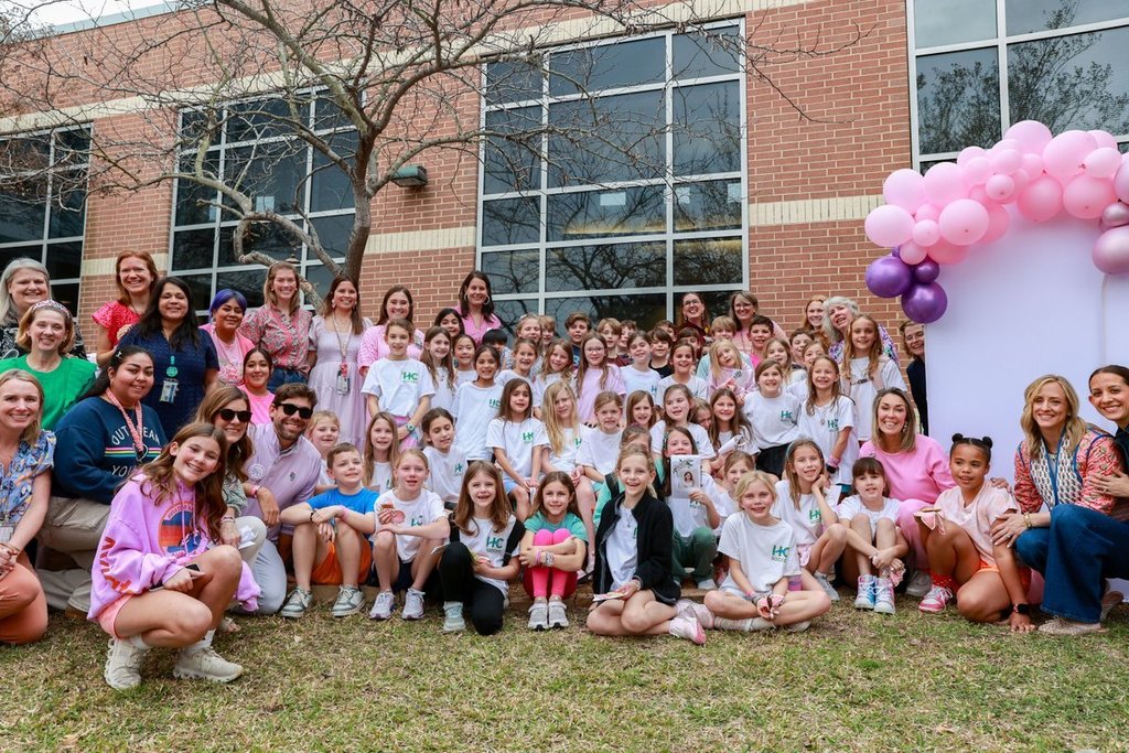 Many people in white t-shirts pose for a group photo outside a building with large windows.