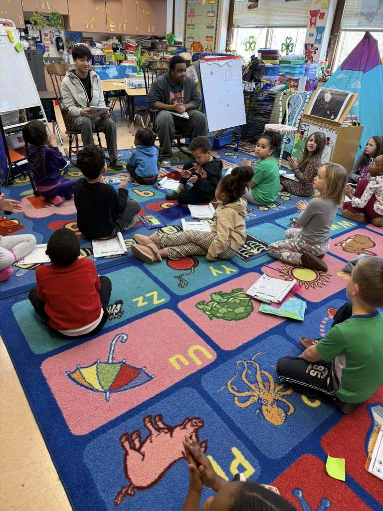Adults reading to young students in a classroom. 