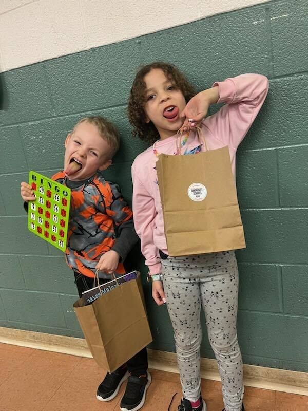 Two students sticking their tongues out and holding goodie bags and one student is holding a bingo board.   