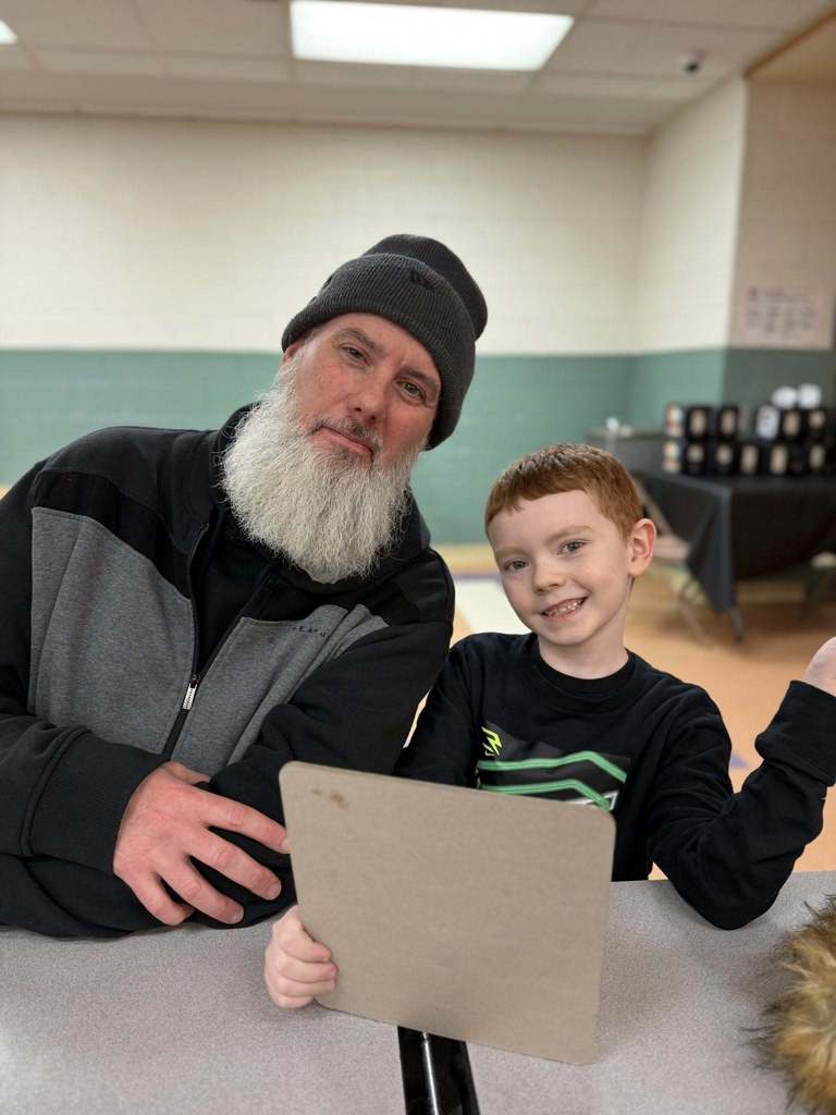 A man and boy smiling while the boy hold a board. 