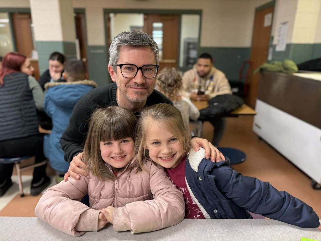 A man hugging two young girls and they are all smiling. 