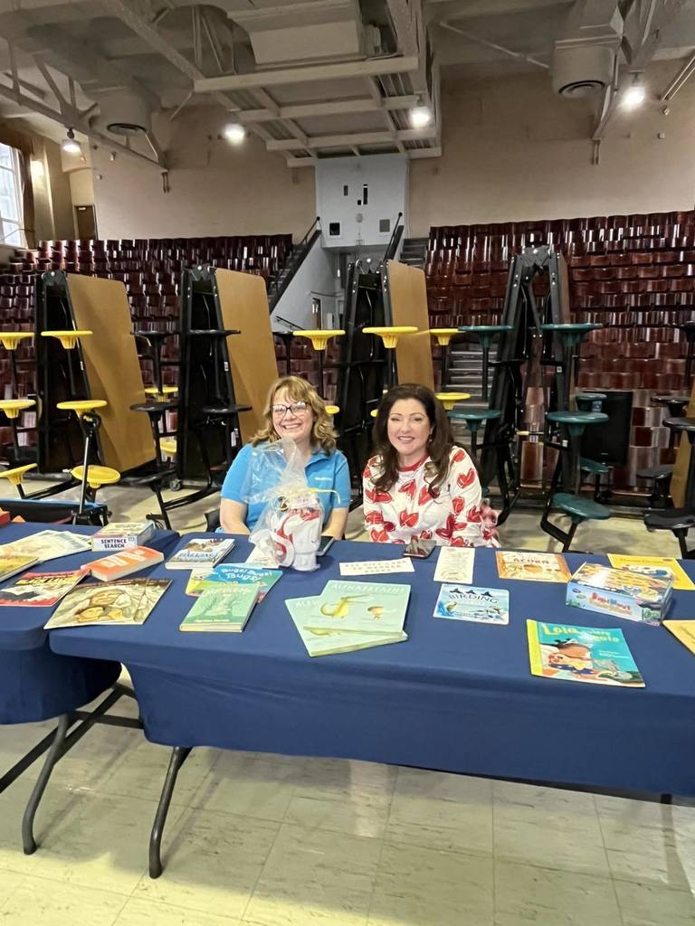 Two women sitting behind a long table with books on it.