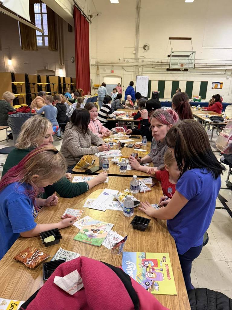 Parents and students playing games, eating snacks, and talking in a school cafeteria.