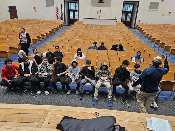 A man talking to students in an auditorium at school.