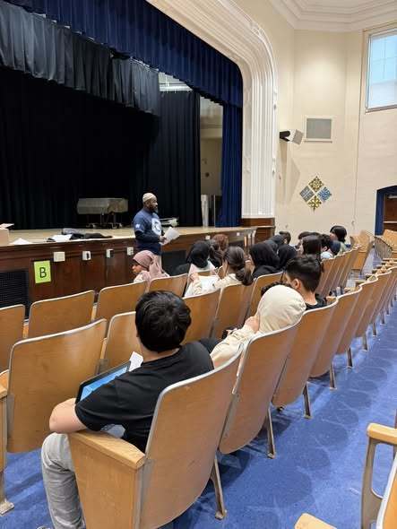 A man talking to students in an auditorium at school.