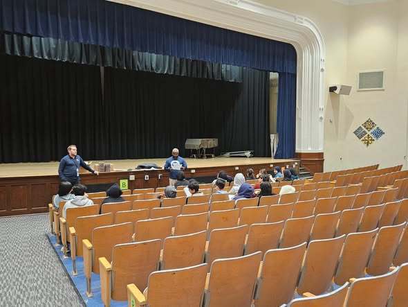 Men talking to students in an auditorium at school.