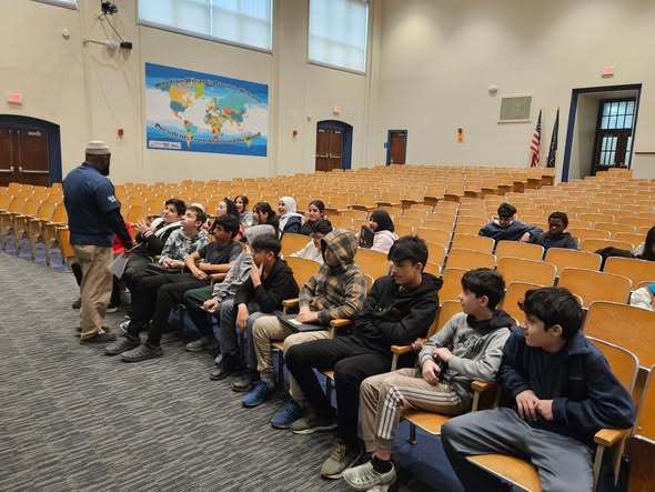 A man talking to students in an auditorium at school.