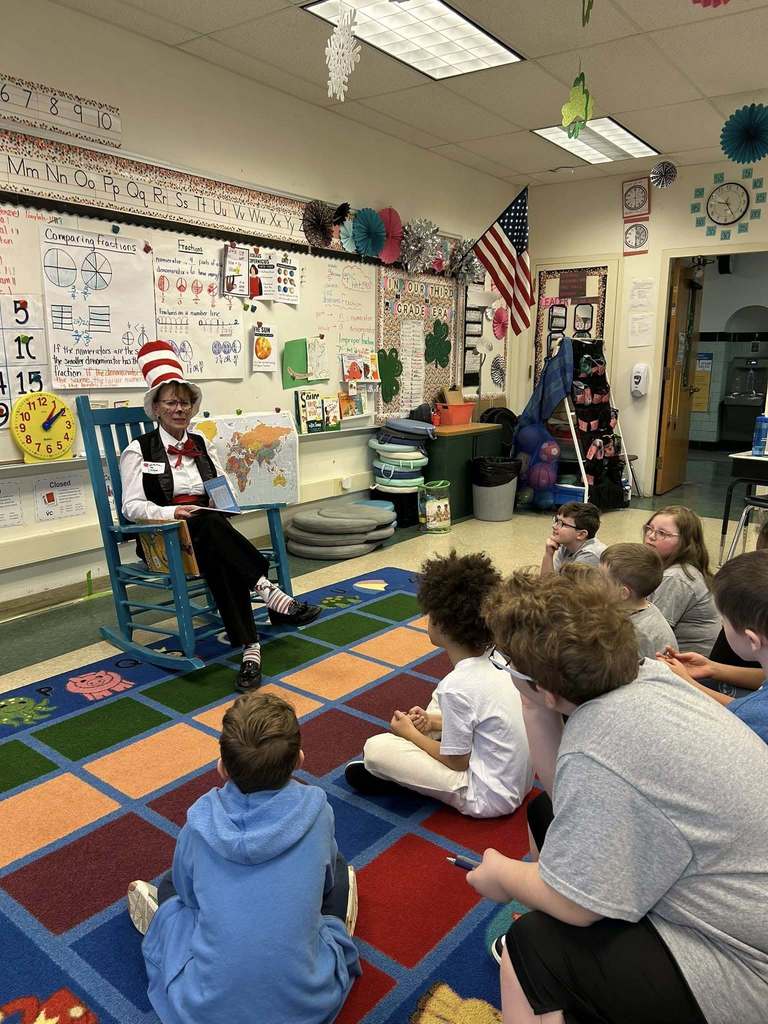 A women dress like Dr. Deuss is reading a book to a classroom of students. 