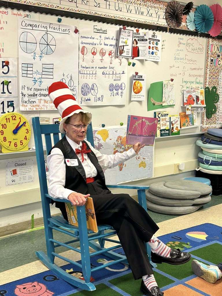 A women dress like Dr. Seuss and reading a book. 
