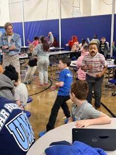 Students wearing fake mustaches and doing work at a table in the cafeteria. 