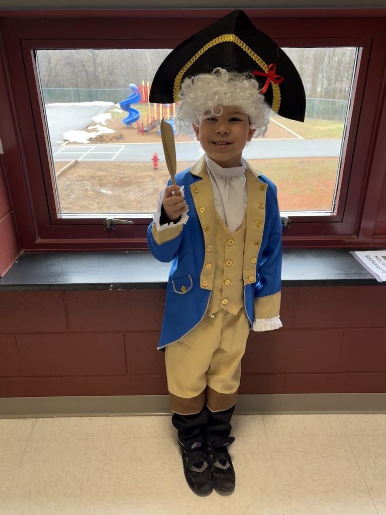 George Washington is holding his quill and smiling.