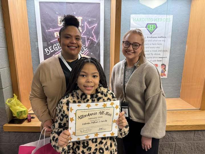Two adults smiling next to a girl who is holding her February Attendance All Star cirtificate.