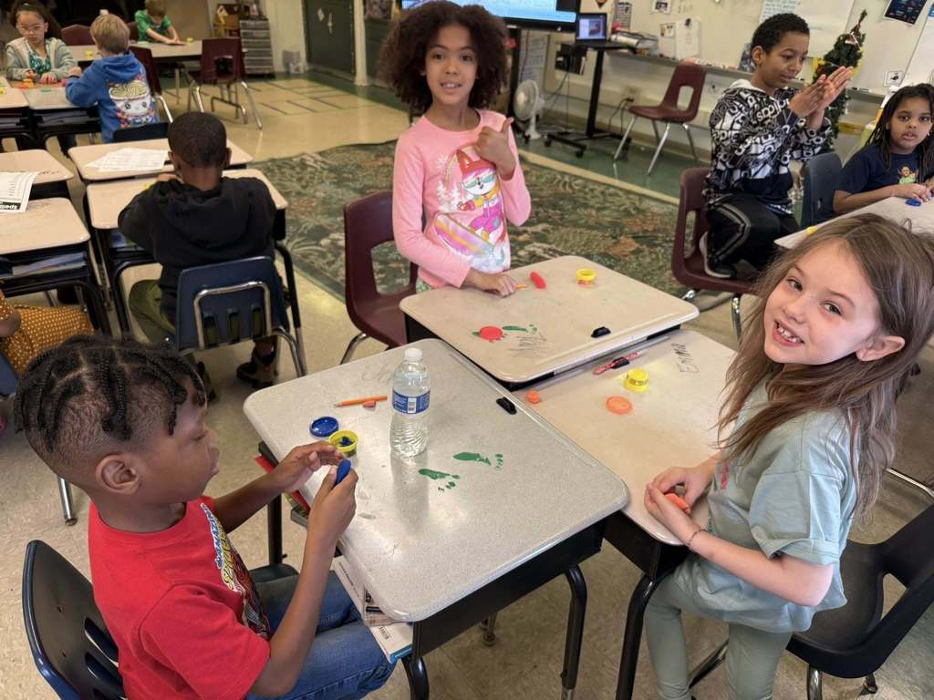 Kids playing with playdough on tables that has green foot prints on it. 