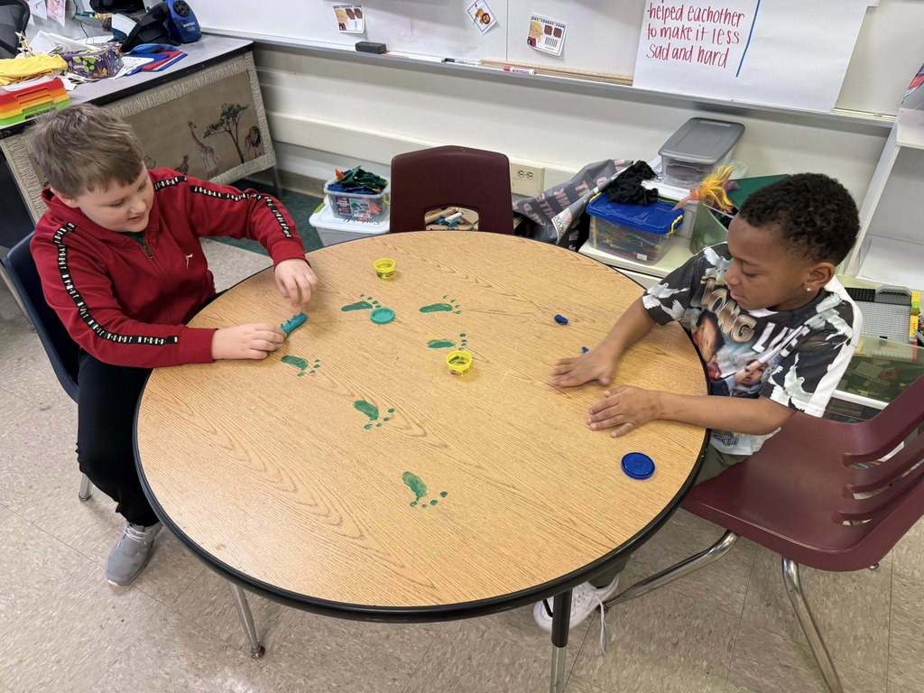 Kids playing with playdough on a table that has green foot prints on it. 