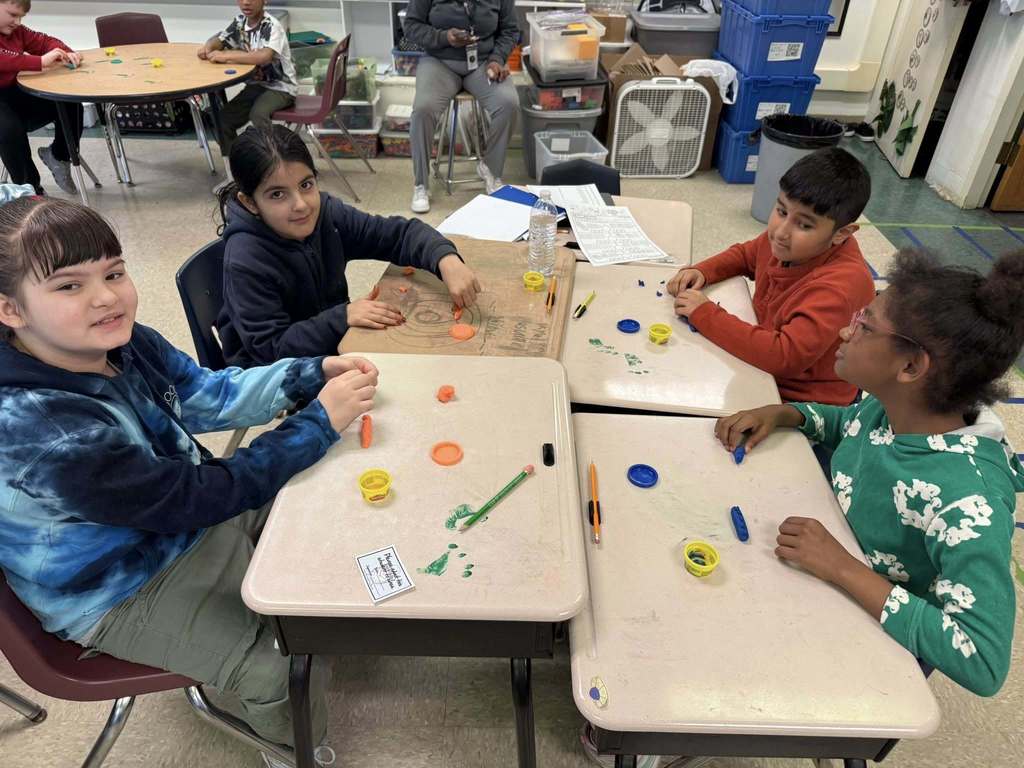 Kids playing with playdough on tables that has green foot prints on it. 