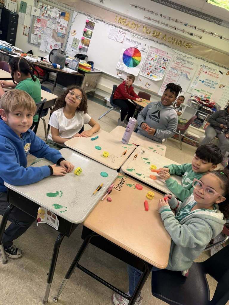 Kids playing with playdough on tables that has green foot prints on it. 