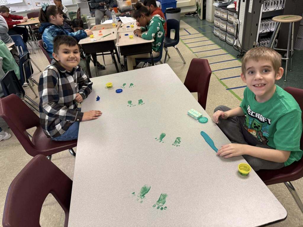 Kids playing with playdough on tables that has green foot prints on it. 