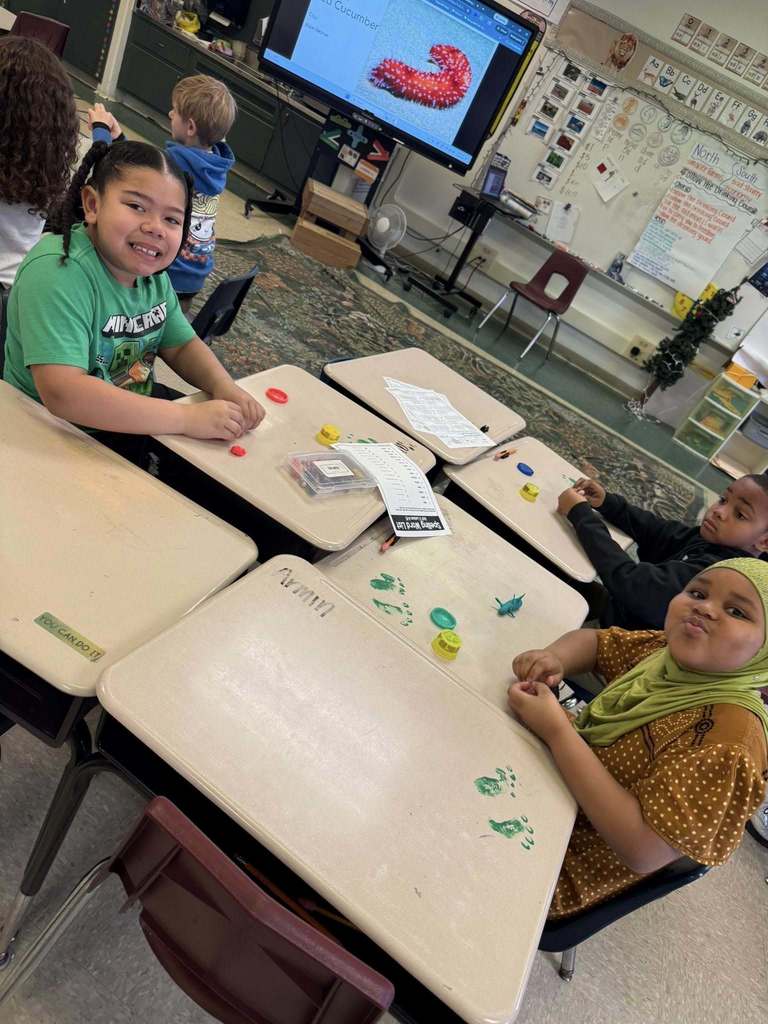 Kids playing with playdough on tables that has green foot prints on it. 