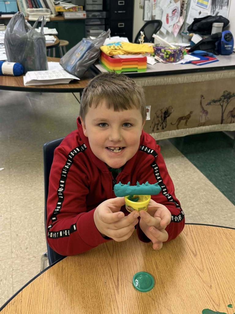 A kid in a red hoodie playing with green playdough.