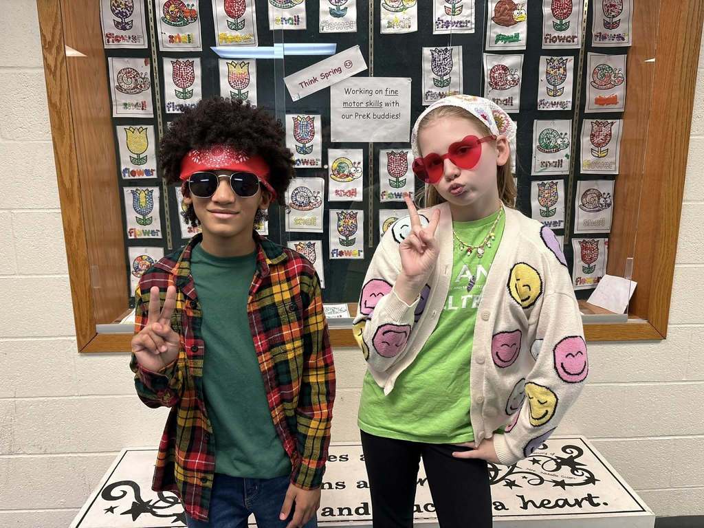 A young boy and girl wearing green shirts, glasses, and bandanas while they hold two fingers up as a peace sign. 
