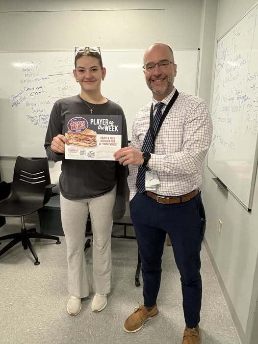 A young girl holding a certificate for Player of the Week with her principal who is wearing a striped tie.