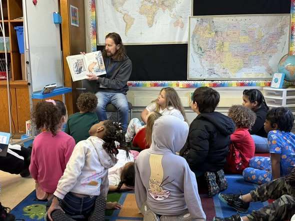 An adult reading a book to students in a classroom.