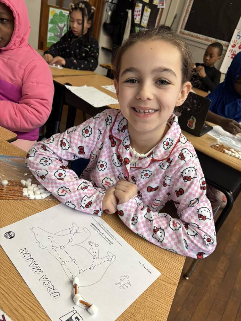 A young student wearing pajamas and smiling in class.