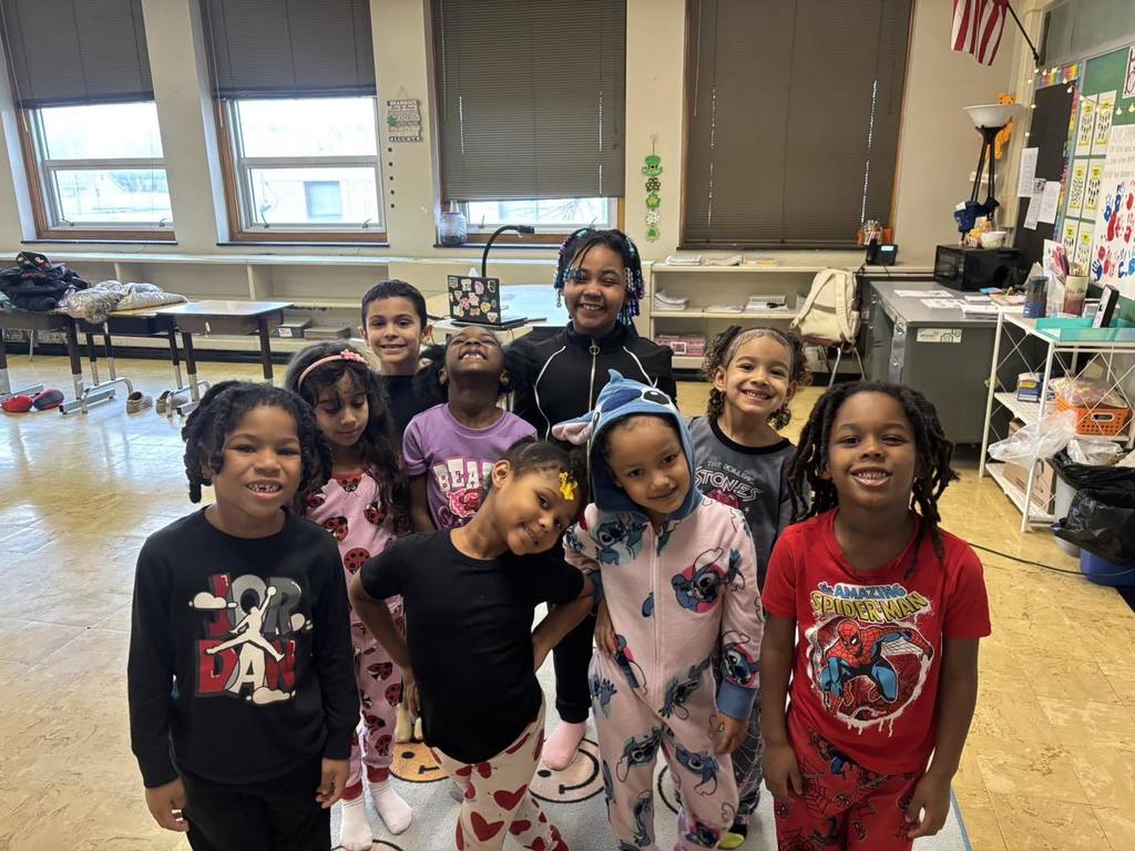 Students smiling in a classroom and wearing pajamas.