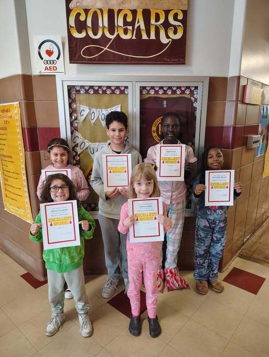 Students standing in a hall and holding their awards. 