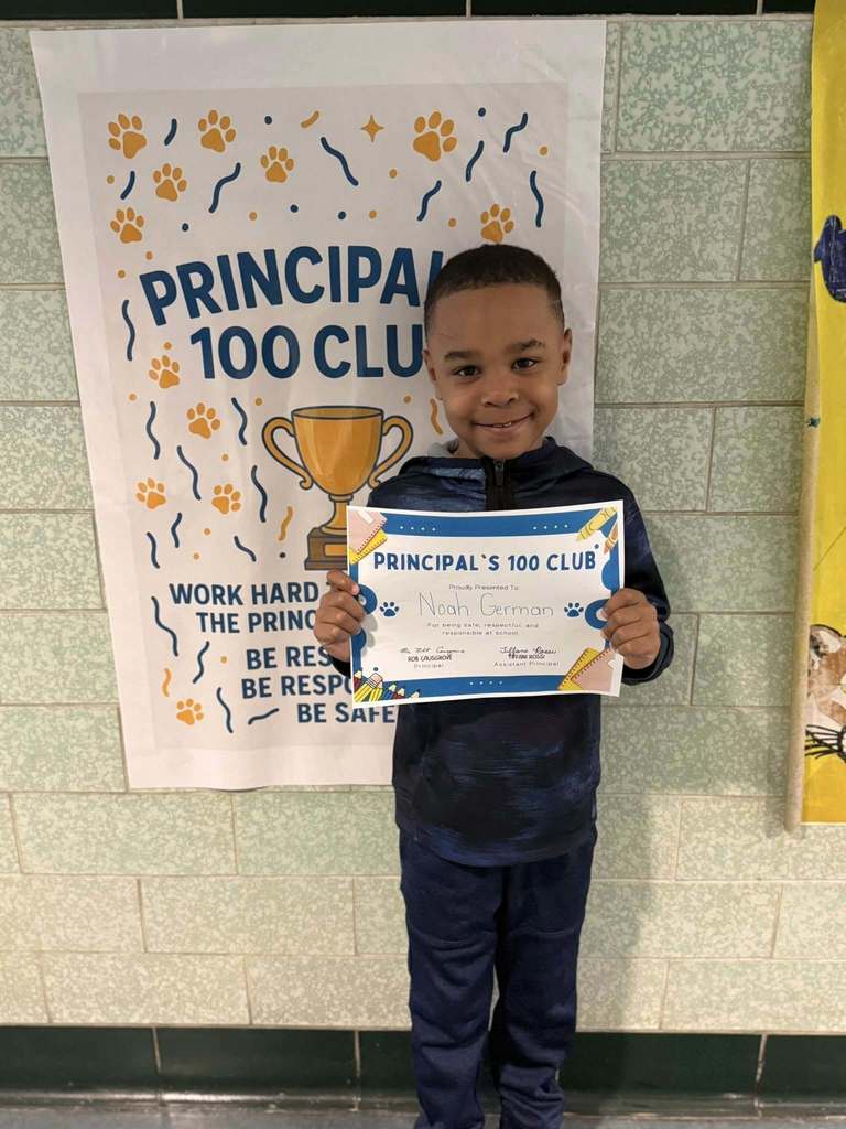 A young boy that is wearing navy blue is holding his Principal's 100 Club certificate. 