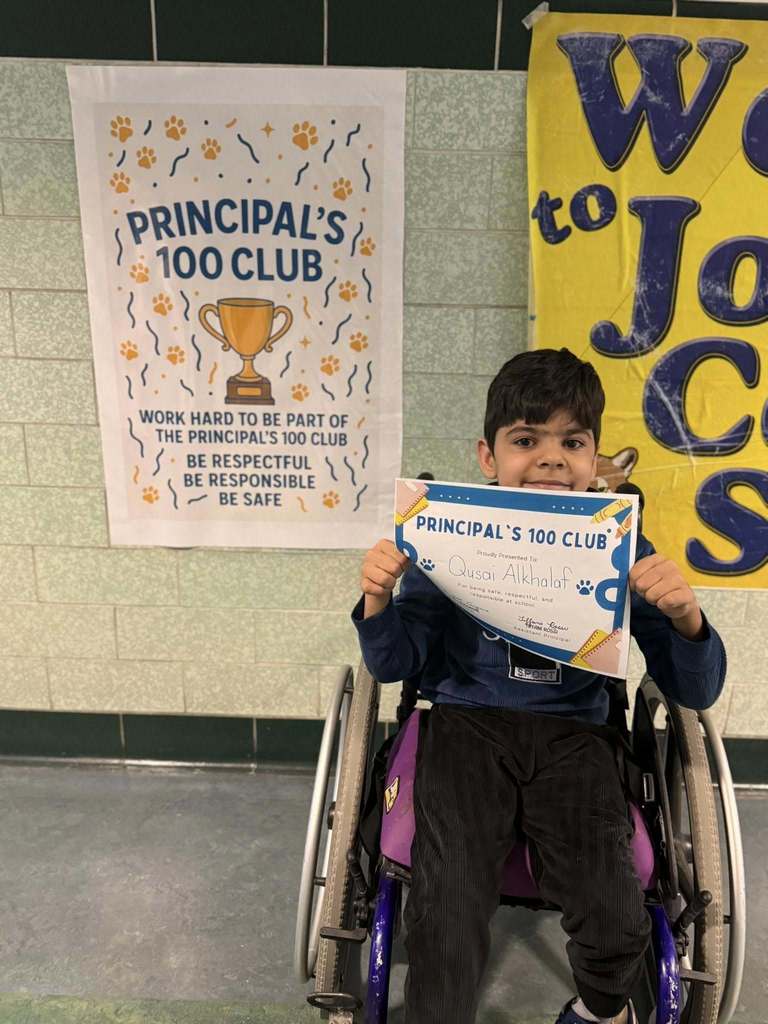 A young boy that is in a wheelchair is holding his Principal's 100 Club certificate. 