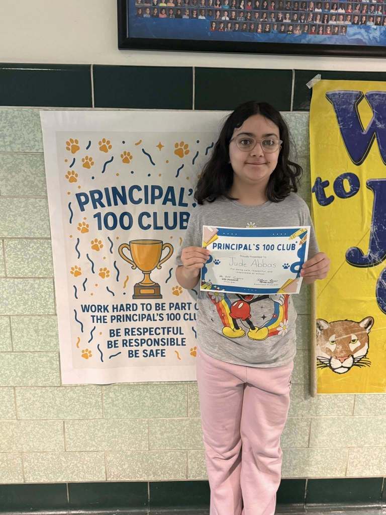 A young girl that is wearing pink pants is holding his Principal's 100 Club certificate. 
