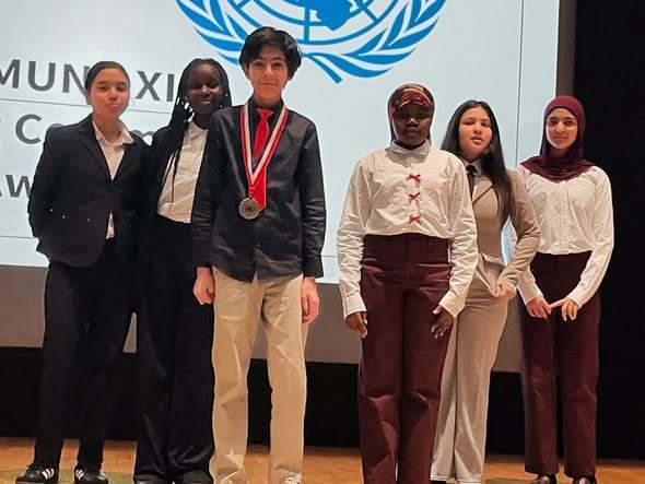 Students standing on stage and dressed professionally while one student wears a medal around his neck. 