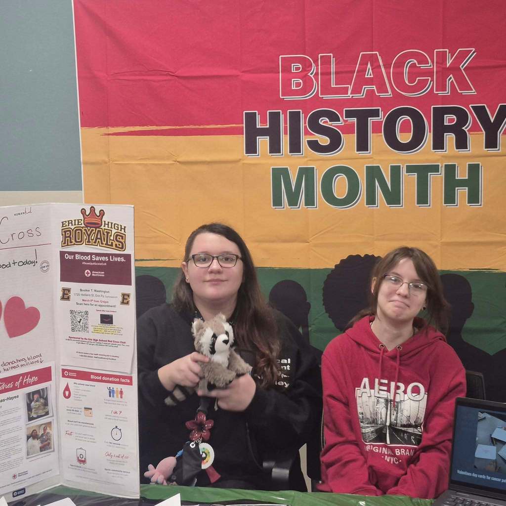Students sitting in front of a banner that says Black History Month at a table and one student is holding a stuffed animal.
