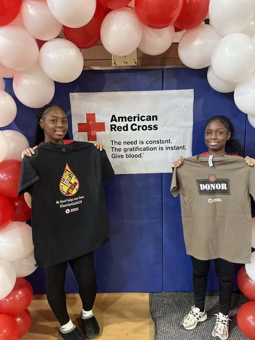Two young girls holding shirts that people can get if they donate blood.