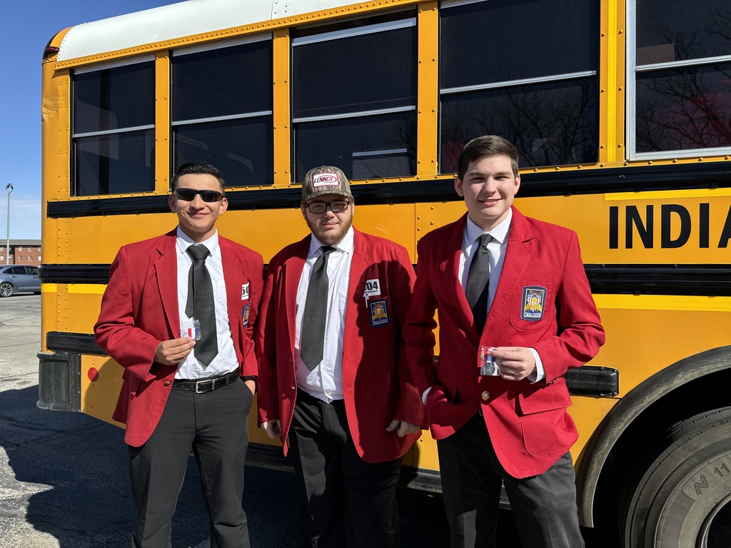 Three men in red blazers and black ties stand in front of a yellow school bus.